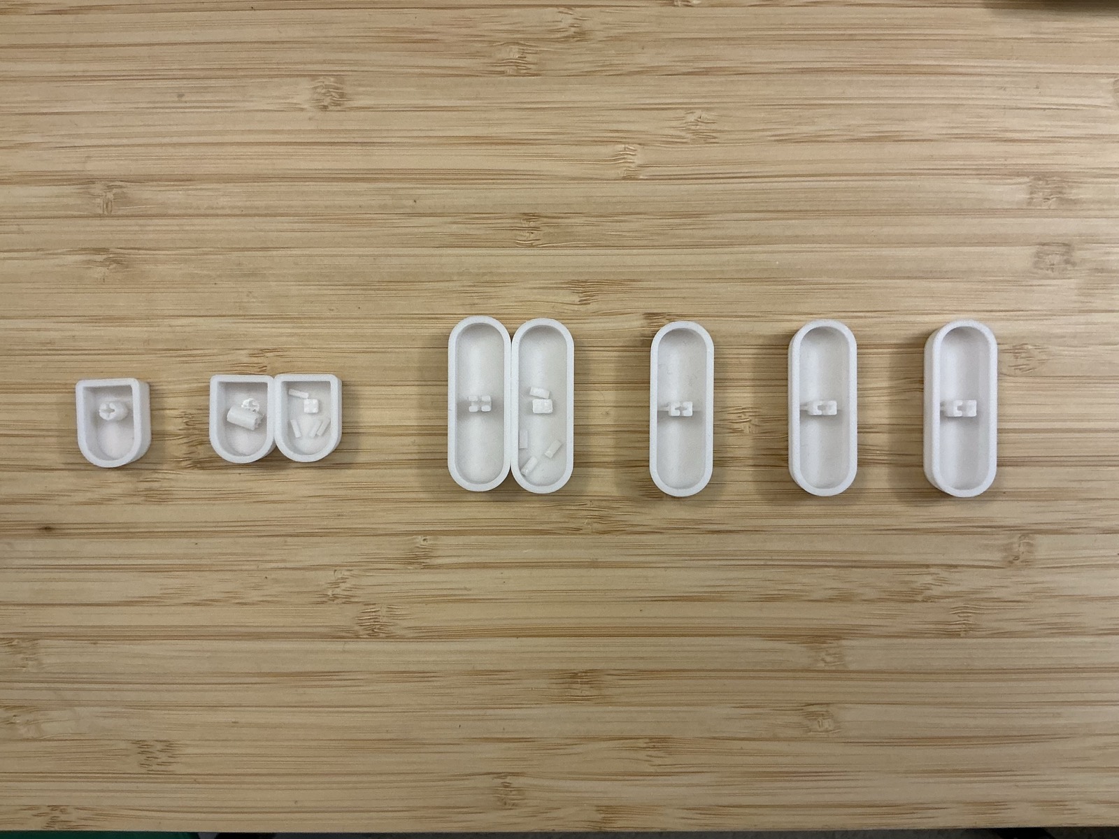Six printed keycap shells laid in a row, upside down, showing successive revisions of the internal gripping fingers